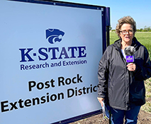 Sandra Wick Crop Production Agent standing next to a sign Post Rock Extension sign