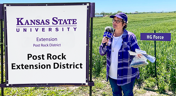Sandra Wick, Crop Production Agent in the field standing by the Post Rock Extension Plot sign
